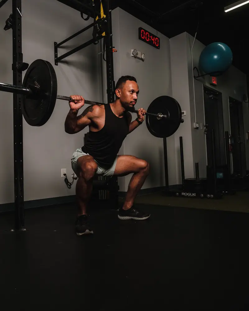 Man lowering into a barbell back squat in a dark gym