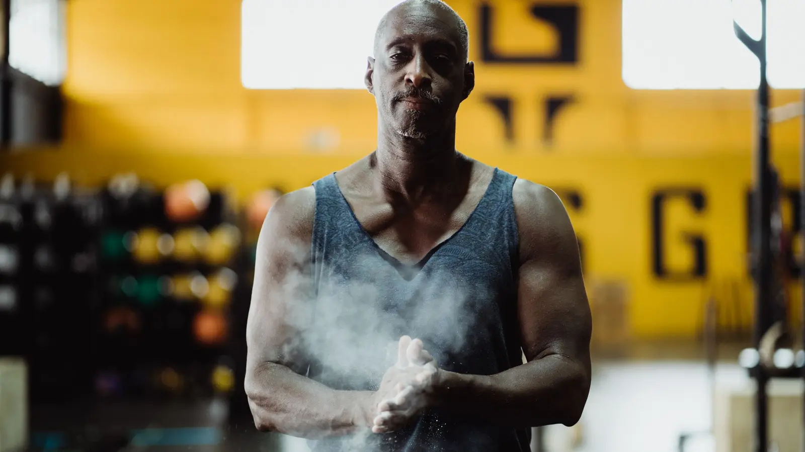 Lifter chalking his hands on the gym floor, a cloud of chalk dust in the light